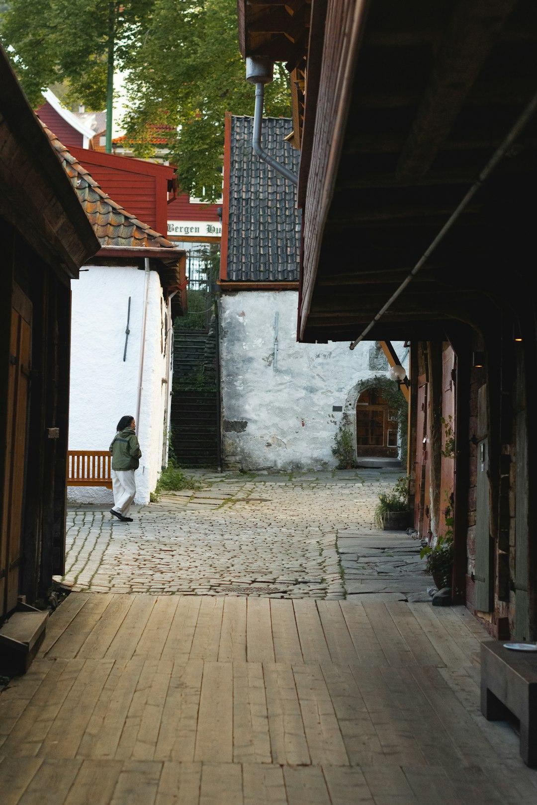 Osoba spacerująca wąską uliczką wśród starych budynków w Bergen, Norwegia.