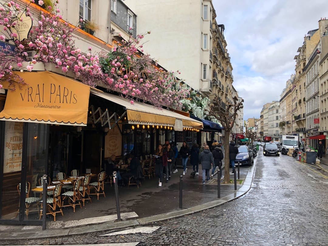 Paryska kawiarnia "Vrai Paris" na brukowanej ulicy Montmartre z różowymi kwiatami.
