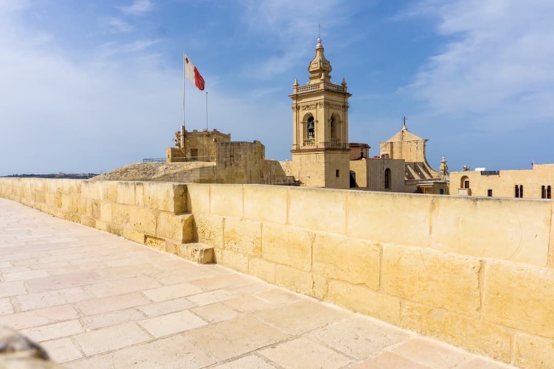 Historyczne budynki cytadeli Gozo z dzwonnicą i flagą maltańską.