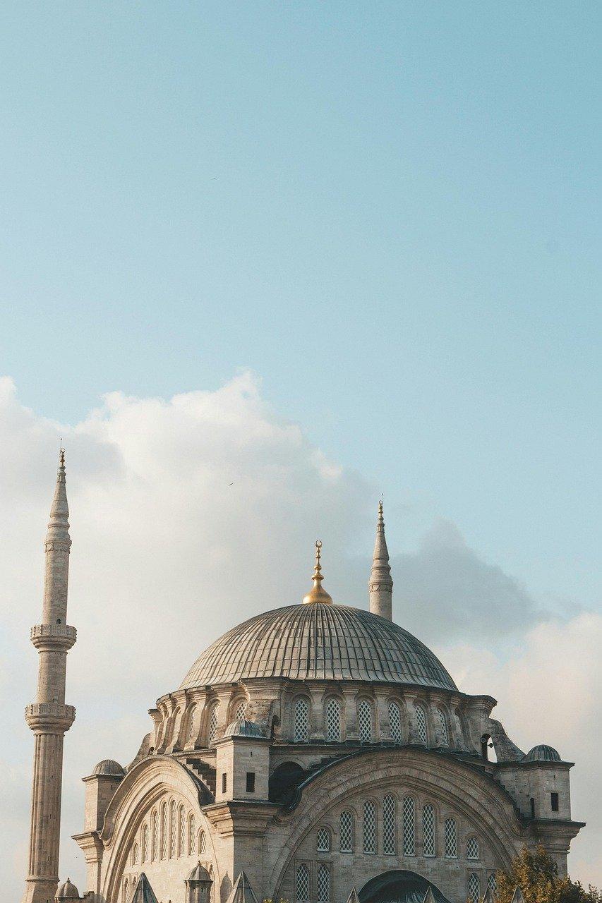 Duży meczet z kopułą i minaretami na tle błękitnego nieba.
