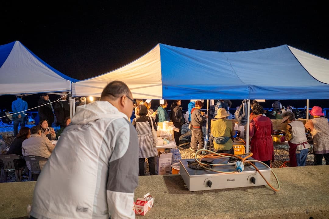 Nocny festiwal jedzenia pod namiotami z ludźmi gotującymi i biesiadującymi.