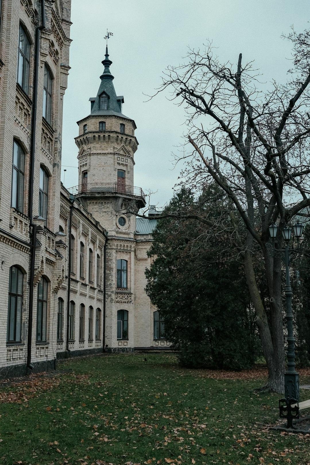 Ceglany budynek z wieżą i szczytem, jesienne drzewa i liście.