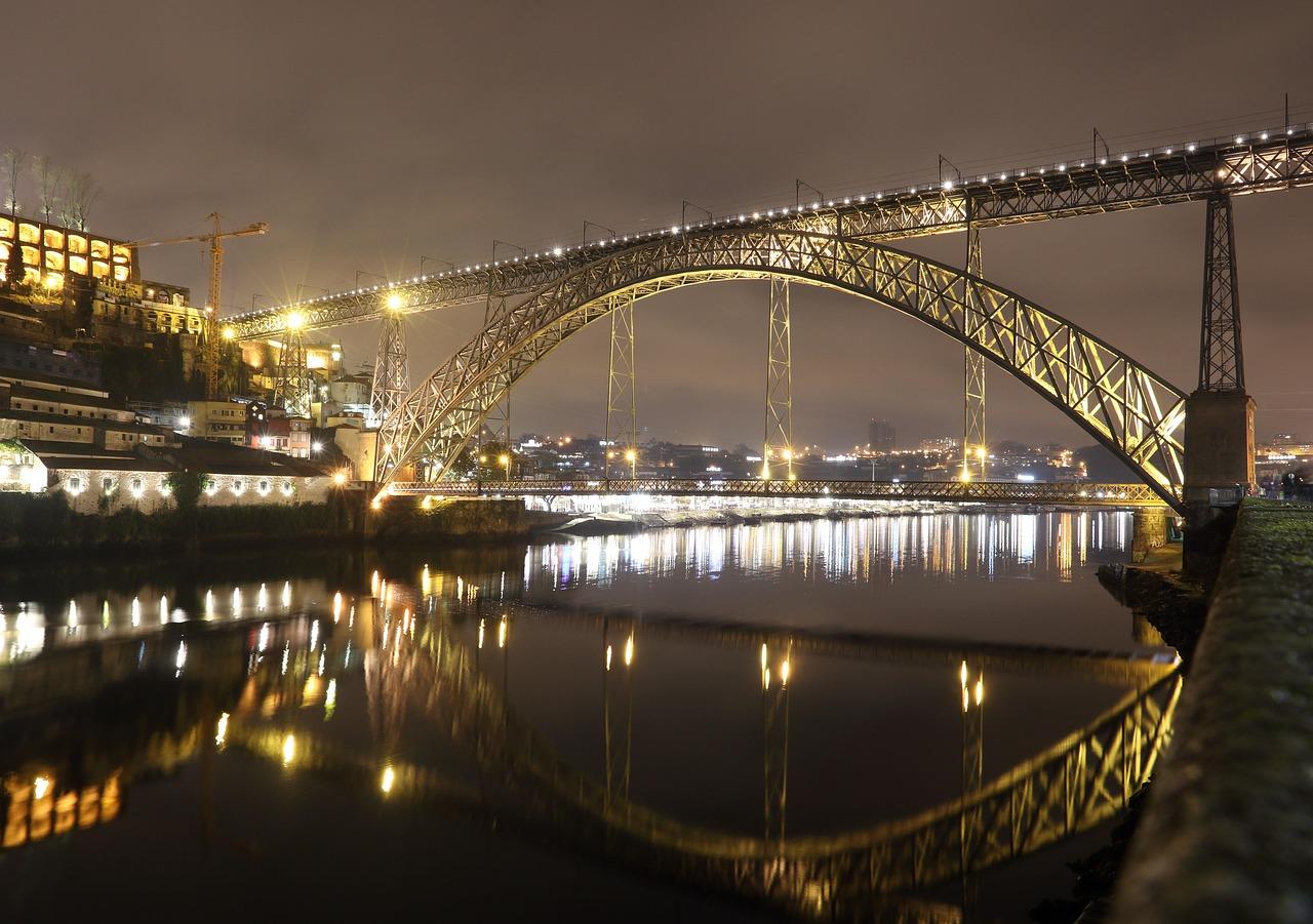 Oświetlony Most Dom Luís I w Porto z odbiciami w rzece Douro.
