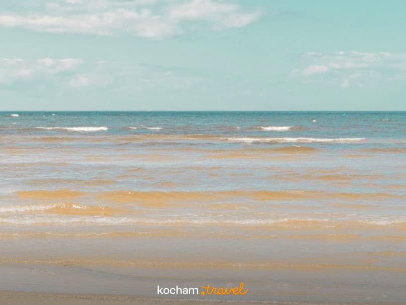 Plaża z falami i piaszczystym brzegiem pod błękitnym niebem.