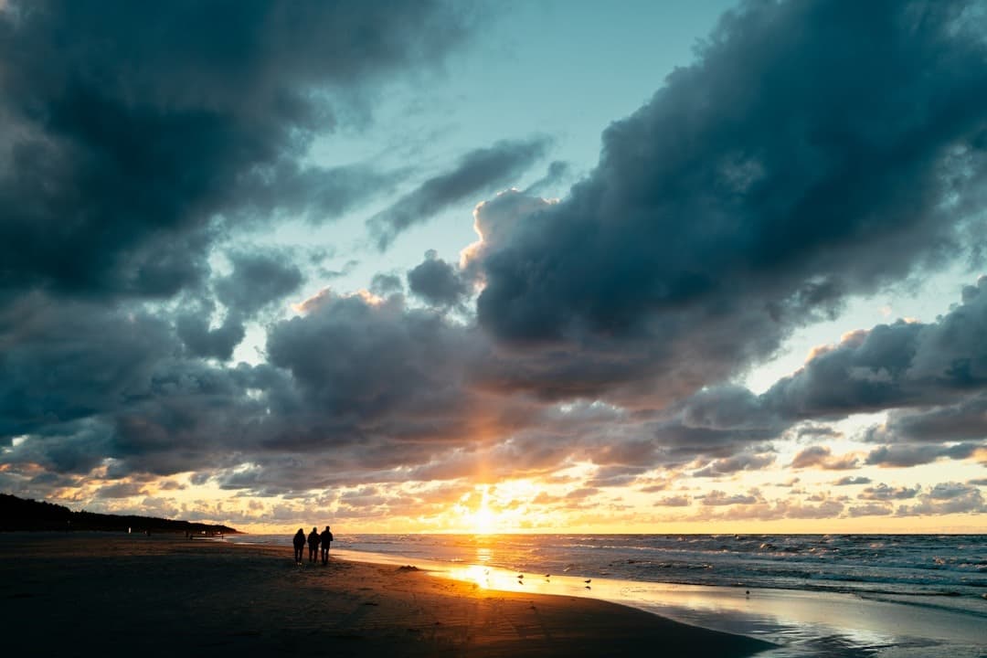 Zachód słońca nad morzem, ludzie spacerujący po piaszczystej plaży.