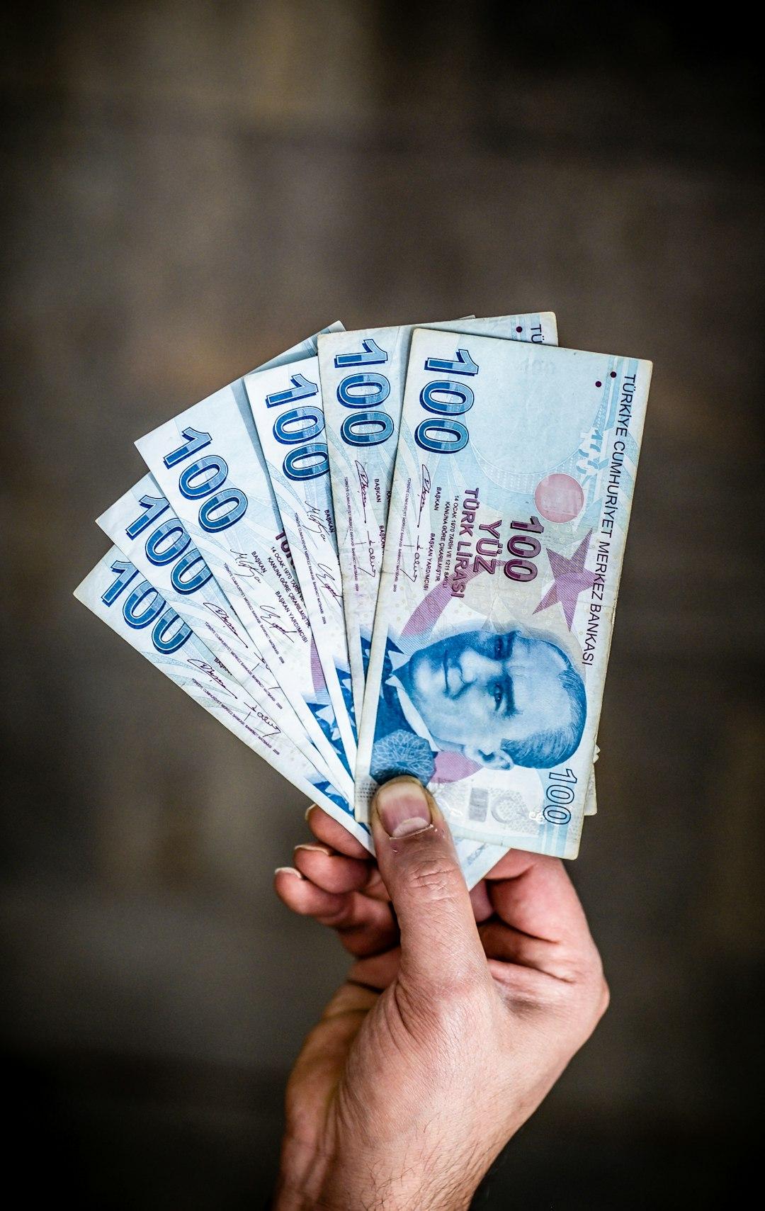 Ręka trzyma fankę banknotów 100 tureckich lirów.