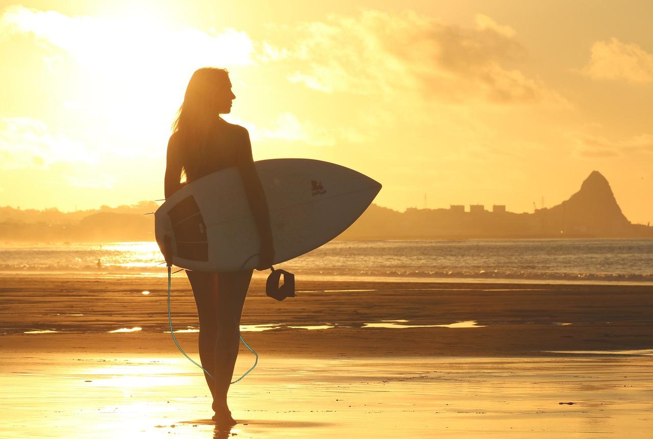 Surferka z deską surfingową na złotej plaży o zachodzie słońca.
