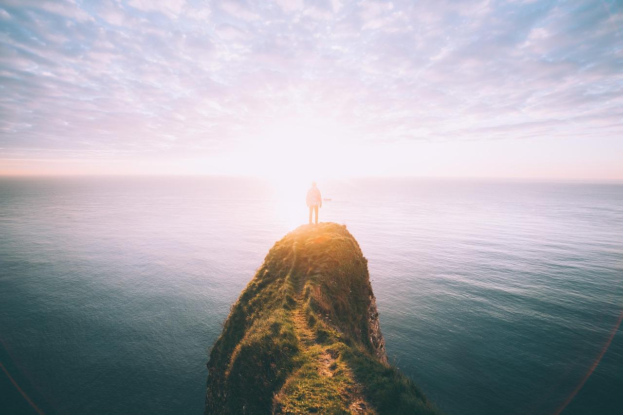 Osoba na szczycie klifu podziwiająca wschód słońca nad oceanem.