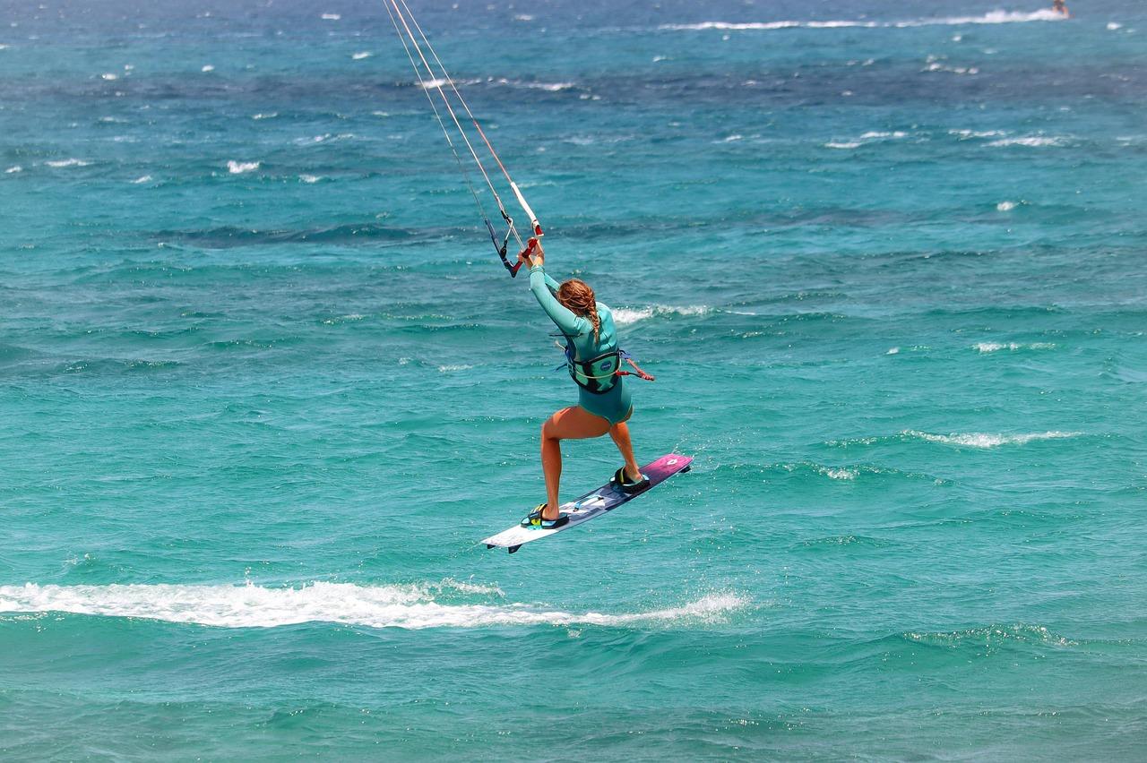 Kobieta kitesurferka w powietrzu nad turkusową wodą.