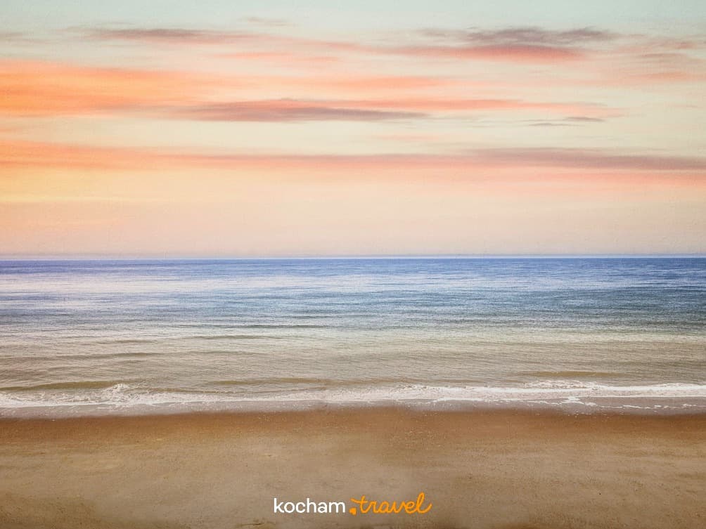 Spokojna plaża, ocean i niebo z pastelowymi chmurami o zachodzie słońca.
