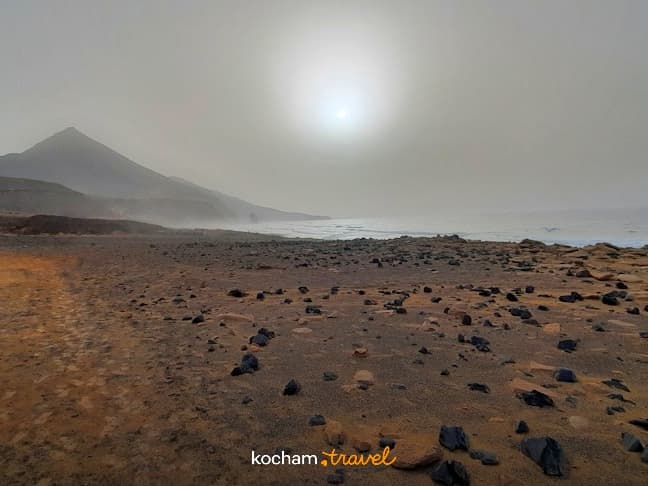 Panoramiczny krajobraz skalistej plaży, mgliste słońce, góry, fale oceanu.