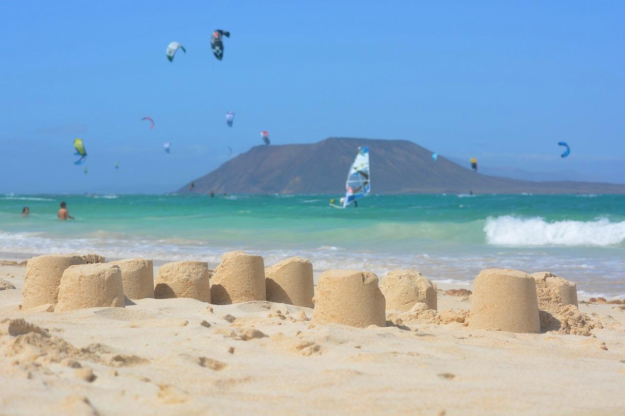 Słoneczna plaża, turkusowe morze, kitesurfing, windsurfing i zamki z piasku.