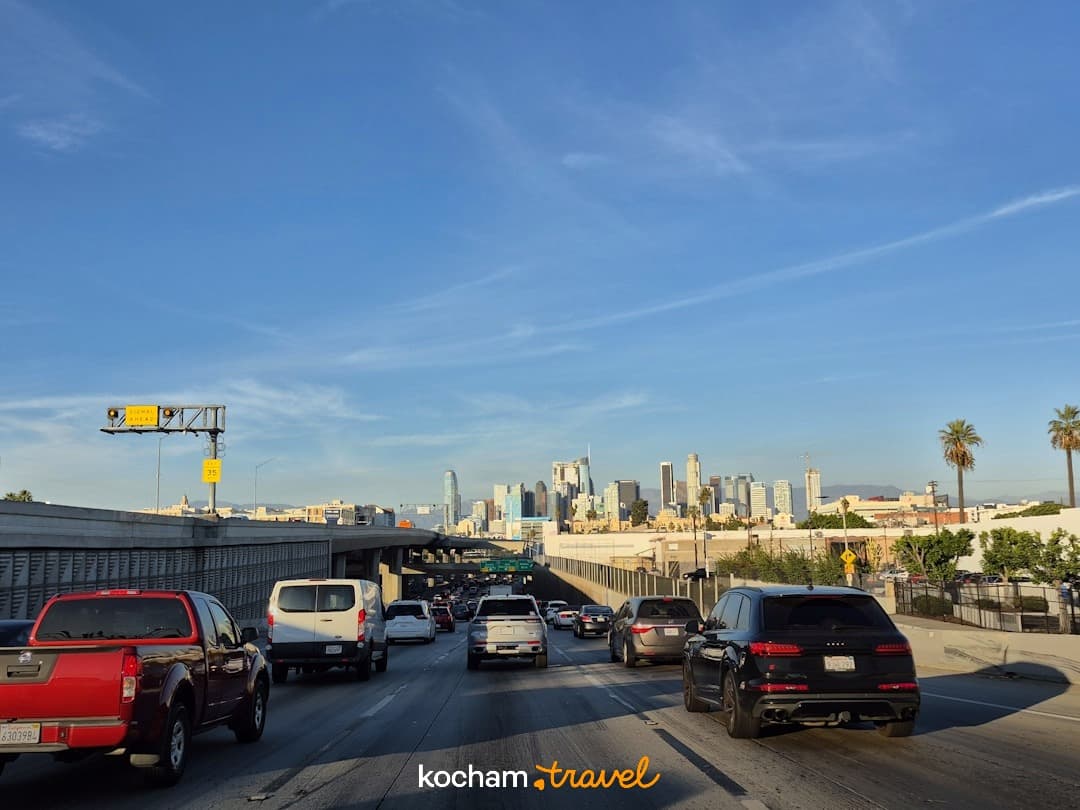 Autostrada w Los Angeles z ruchem samochodowym i wieżowcami w tle.