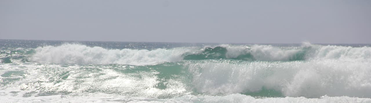 Spienione fale oceanu z turkusową wodą pod jasnym niebem.