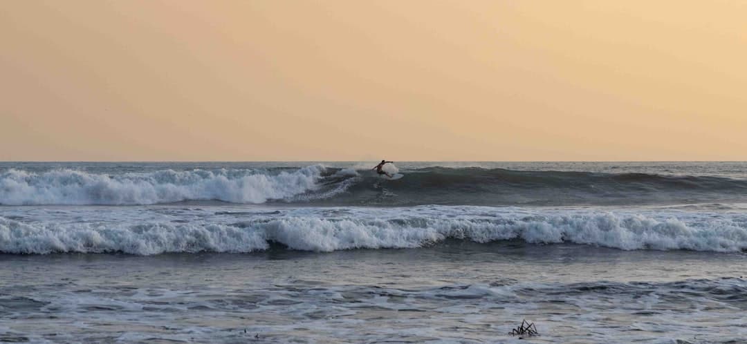 Surfer łapiący falę na oceanie o zachodzie słońca.