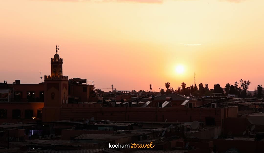 Minaret i miejskie dachy w sylwetce na tle zachodzącego słońca.