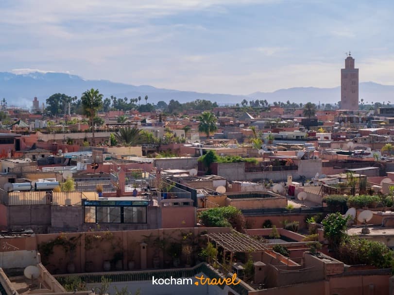 Panorama Marrakeszu z minaretem, dachami i ośnieżonymi górami Atlas.