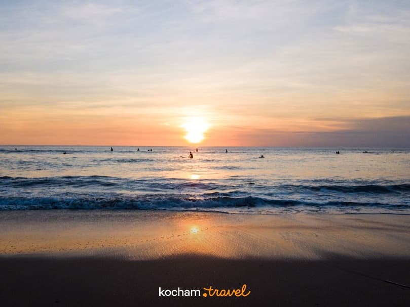 Zachód słońca nad oceanem, plaża, surferzy, ciepłe światło