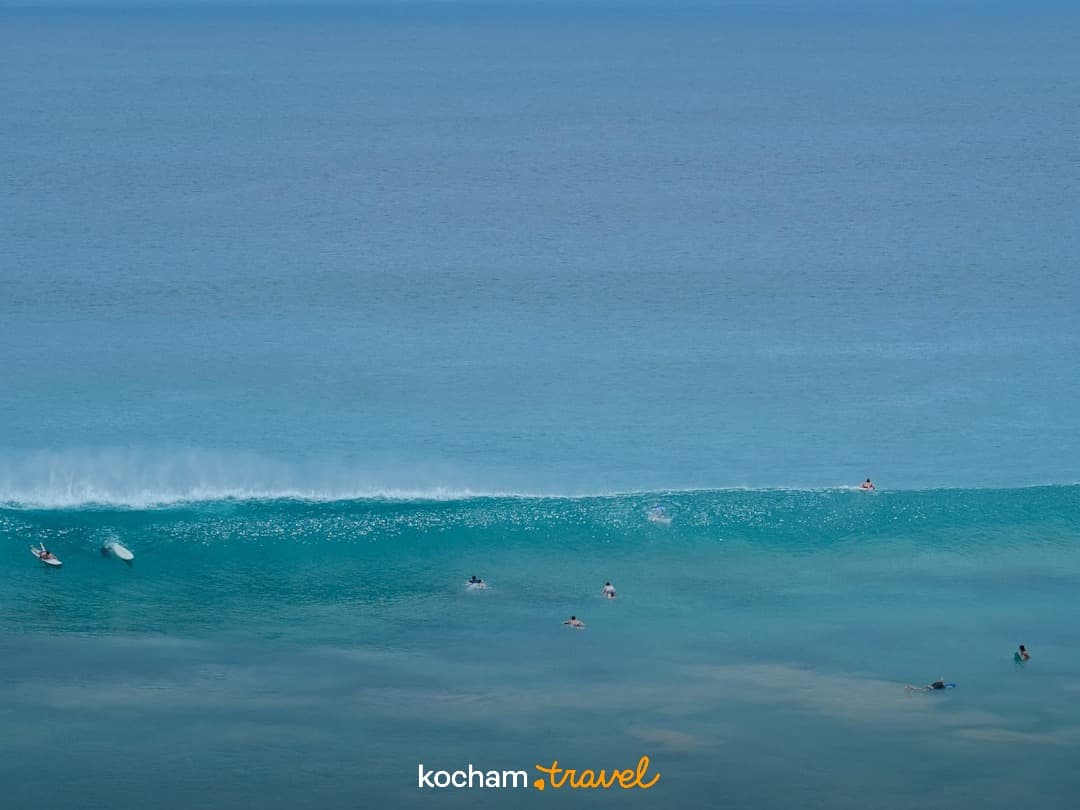 Surferzy na turkusowej wodzie oceanu z falą w słoneczny dzień.