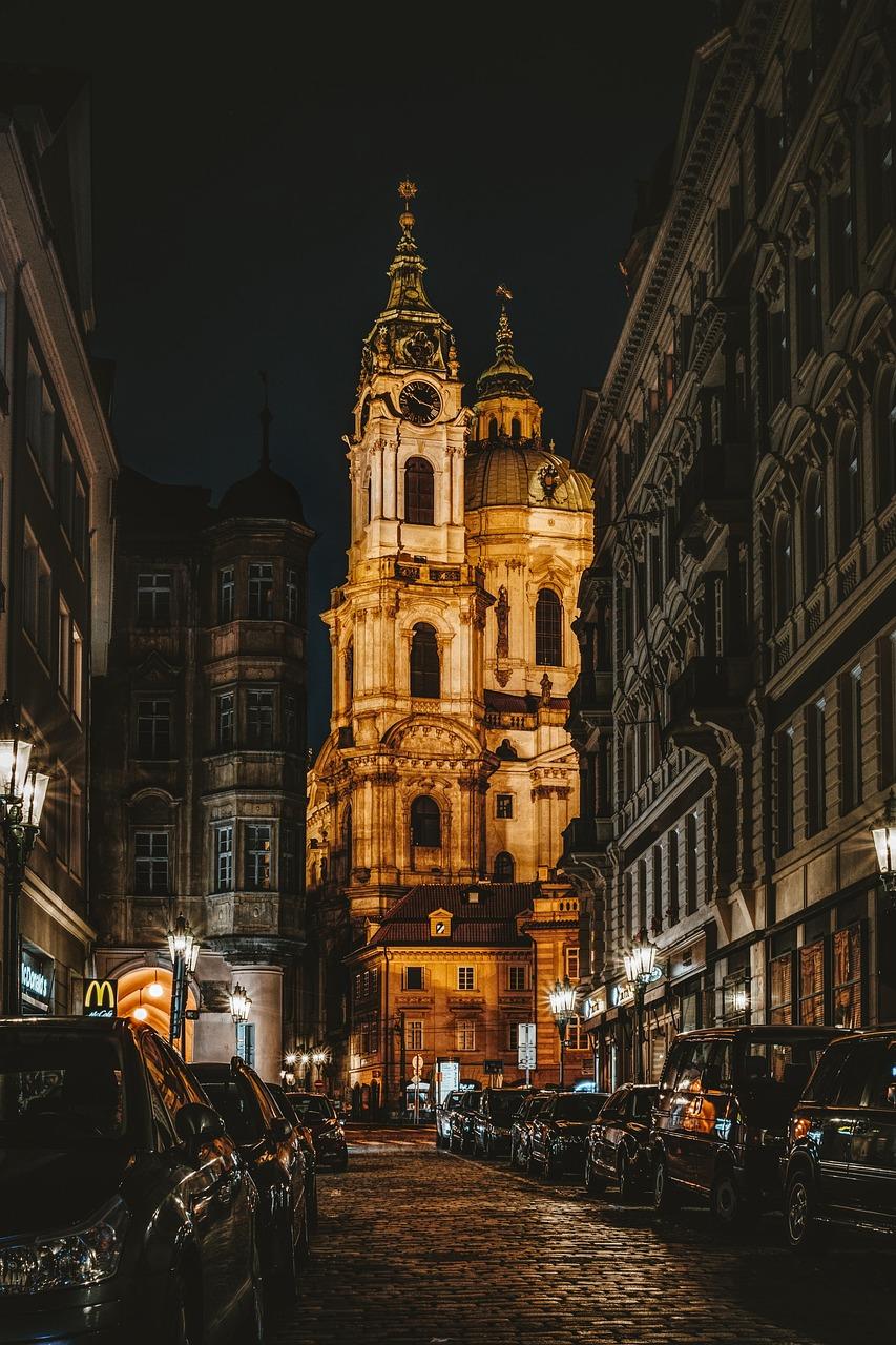 Oświetlony barokowy kościół na brukowanej ulicy Pragi nocą