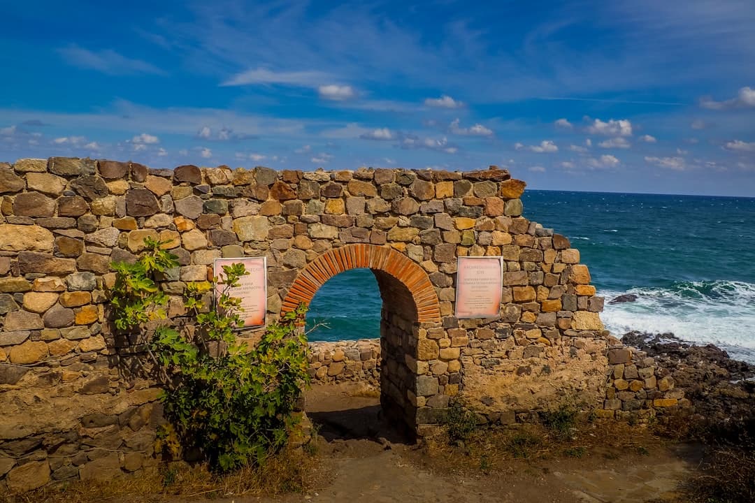 Archeologiczne ruiny kamiennego muru z łukiem nad turkusowym morzem.