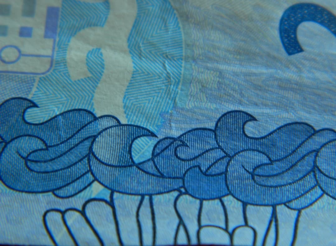 Zbliżenie niebieskiego banknotu z falistymi wzorami i numeracją.