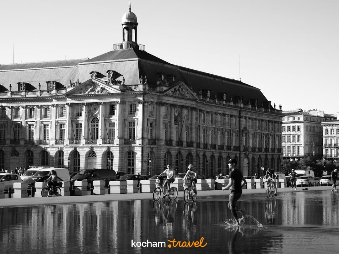 Czarno-biały Pałac Bourse Bordeaux, lustro wody, odbicia, ludzie, rowery.