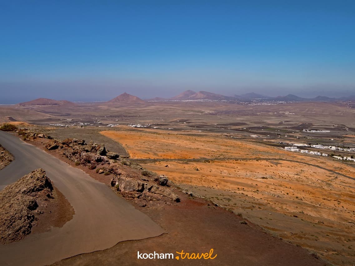 Panoramiczny widok suchego wulkanicznego krajobrazu, droga, góry i zabudowania.