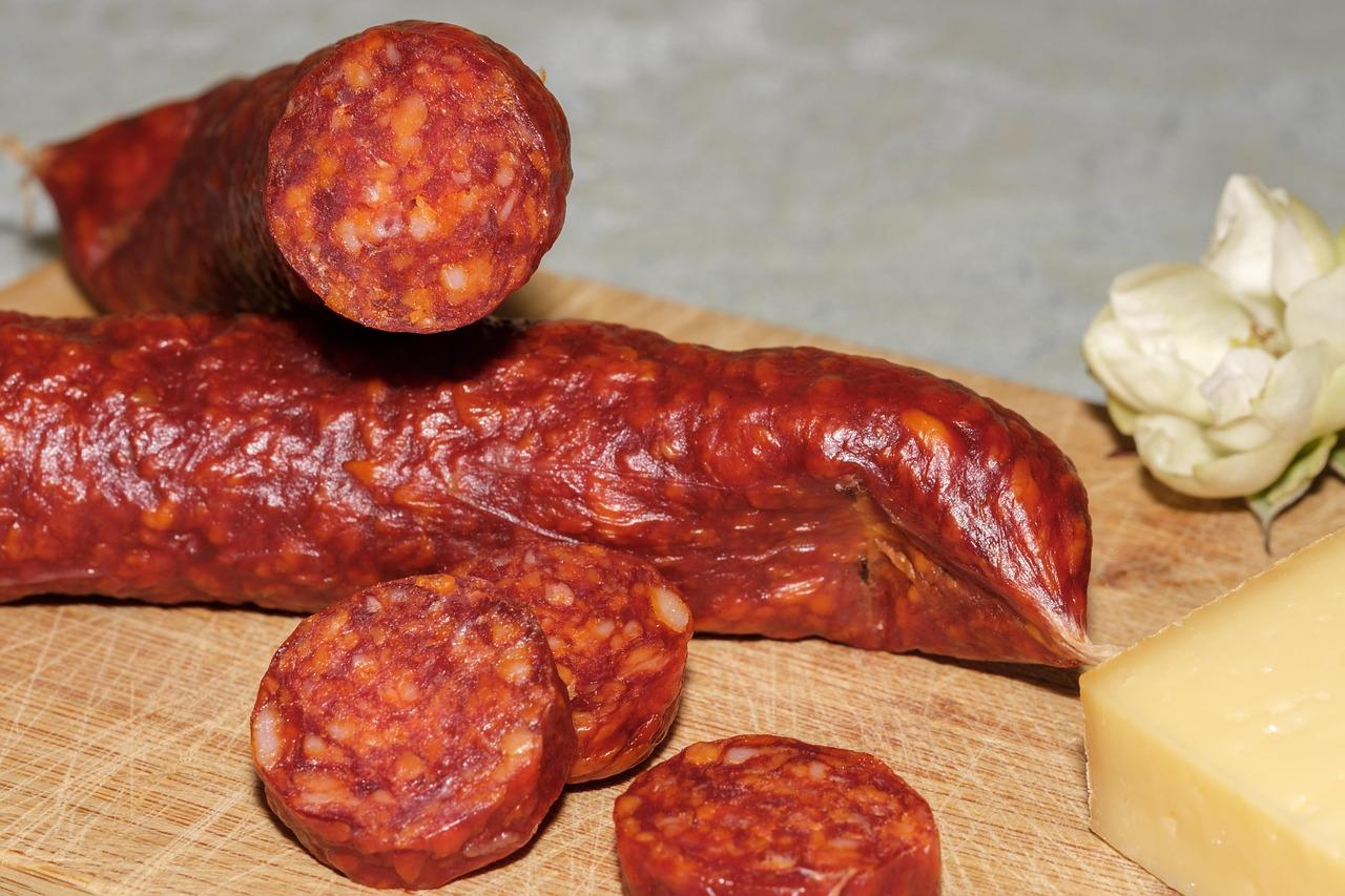 Pikantna czerwona kiełbasa, pokrojona, z żółtym serem na desce.