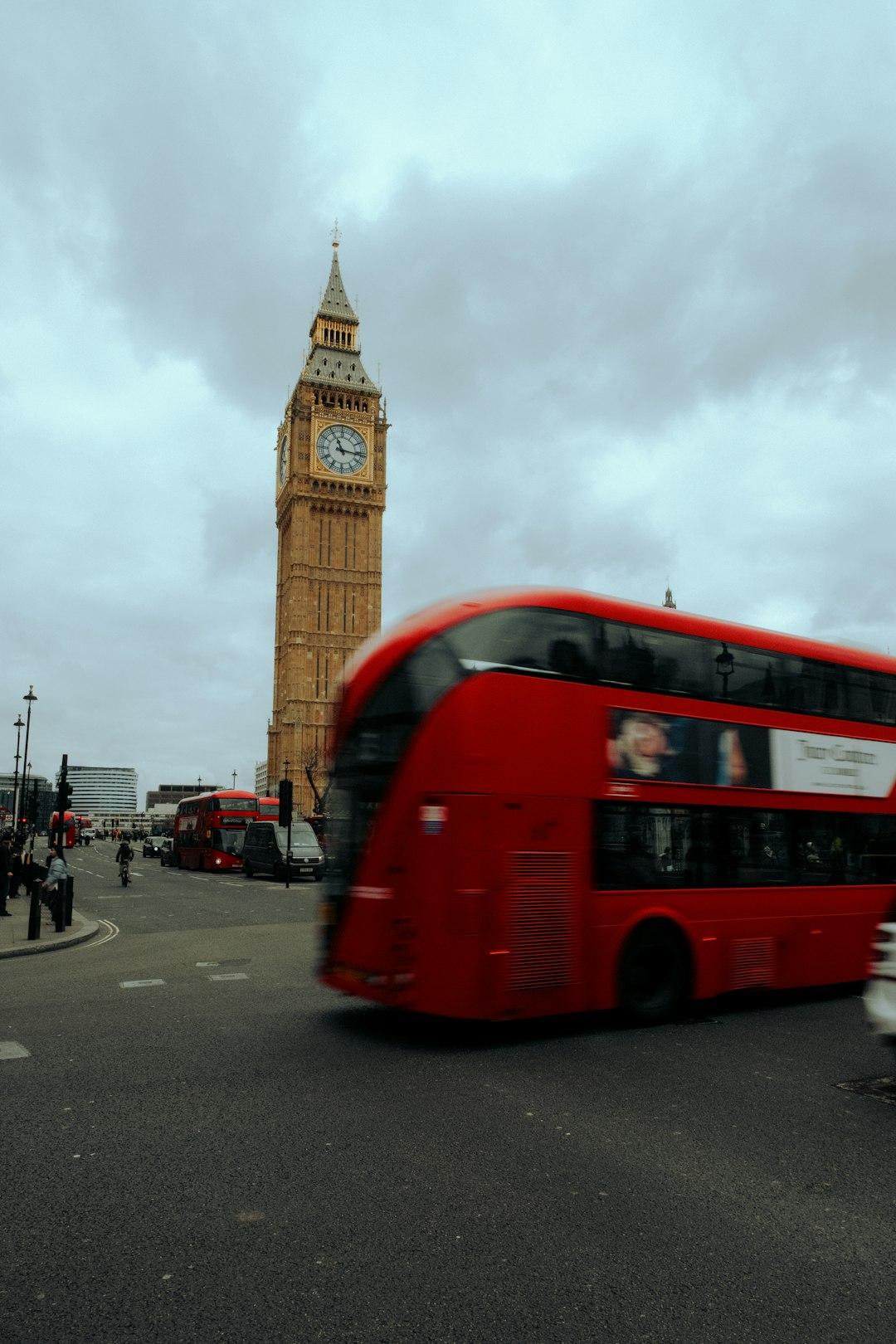 Big Ben i czerwony autobus na ulicy Londynu pod chmurami.