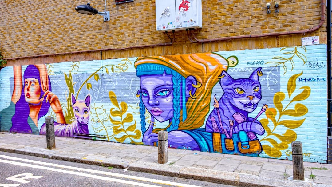 Kolorowy mural z kobietami i kotami na ceglanej ścianie miasta.