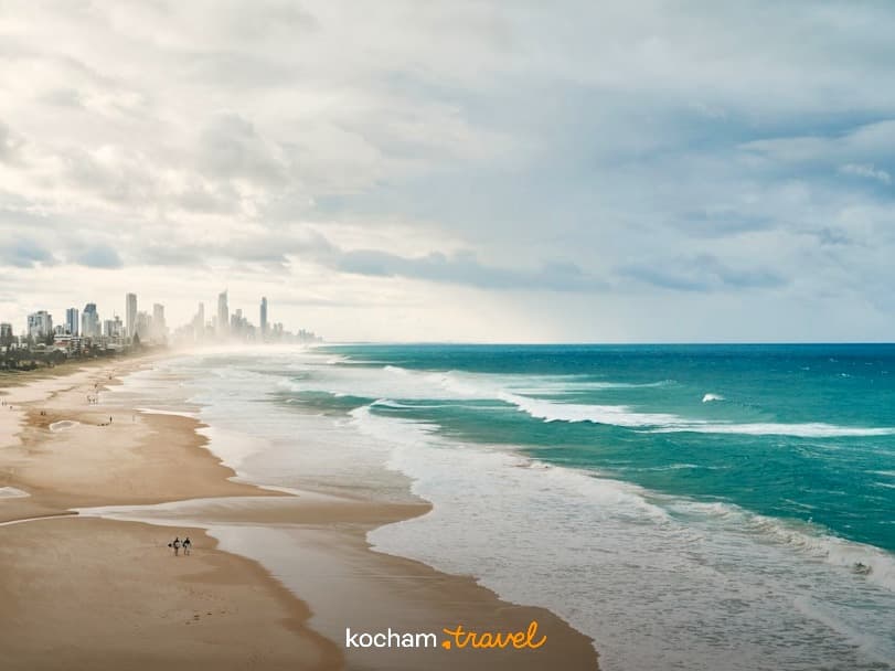 Panoramiczna plaża z turkusowymi falami oceanu i odległym horyzontem miasta.