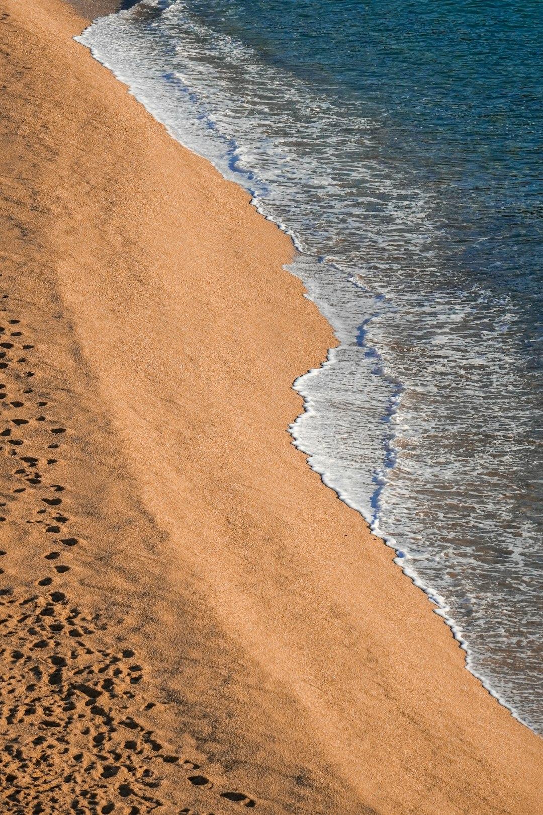 Złota plaża, spienione fale oceanu, ślady stóp na piasku.