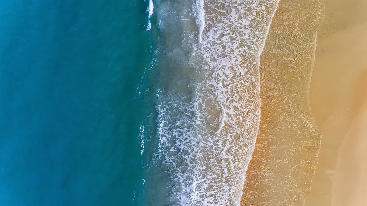Piaszczysta plaża, turkusowy ocean i białe fale z lotu ptaka.