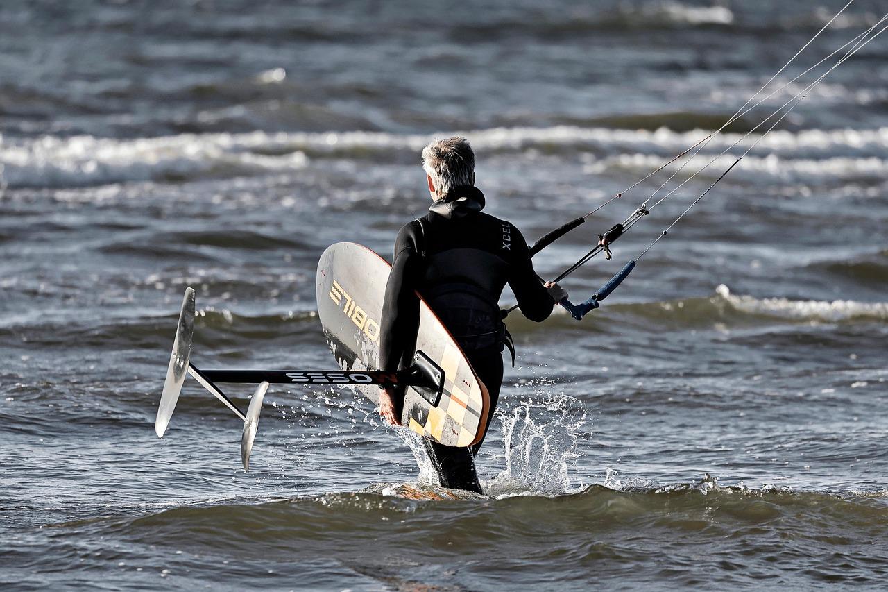 Mężczyzna w piance z deską hydrofoil wchodzi do wzburzonej wody.