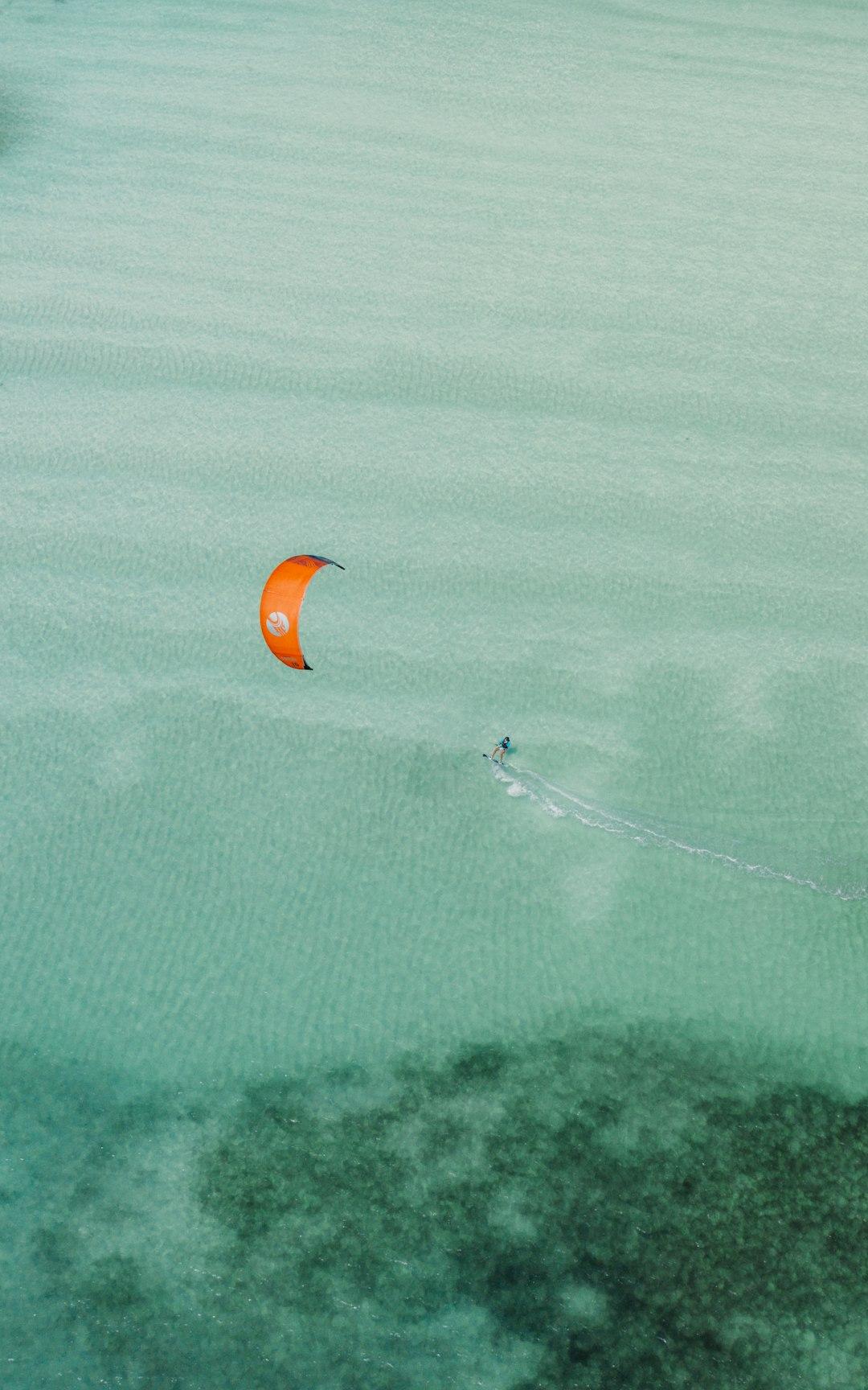 Kitesurfing na krystalicznie czystej, turkusowej wodzie z pomarańczowym latawcem.