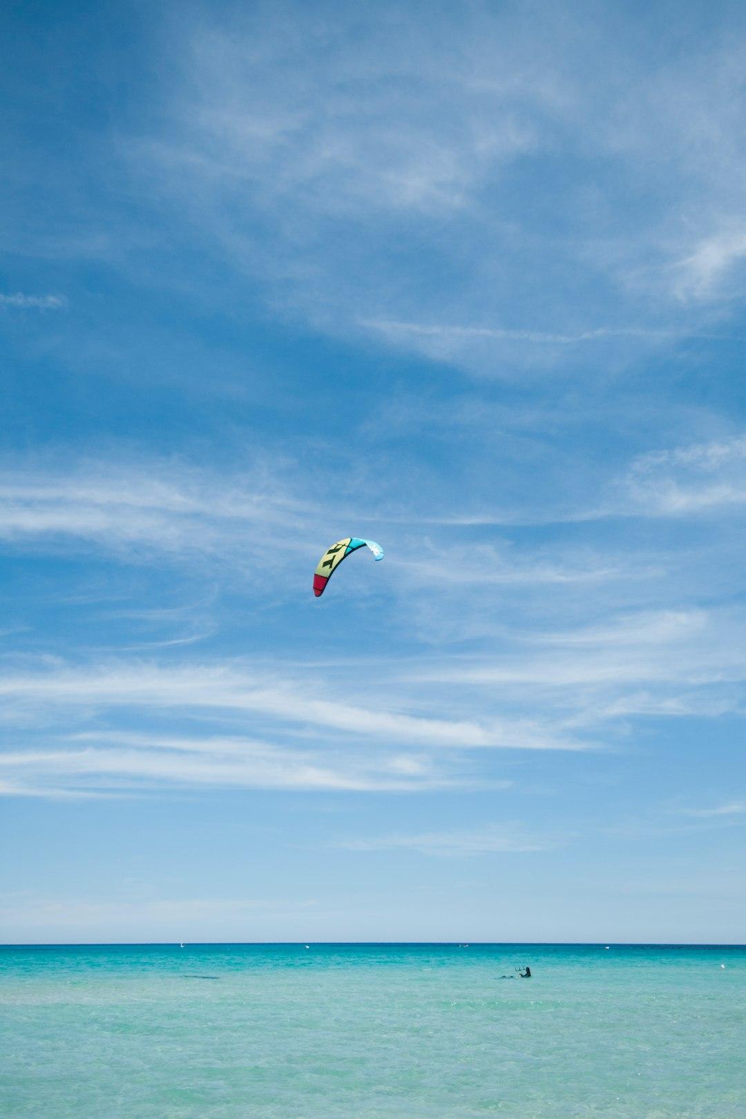 Kolorowy latawiec kitesurfingowy na tle błękitnego nieba i turkusowego morza.