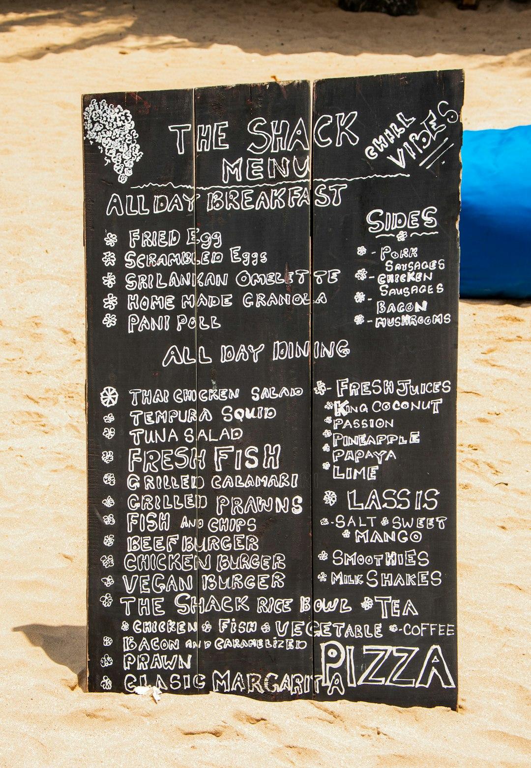 Czarna tablica menu restauracji "The Shack" na piaszczystej plaży.