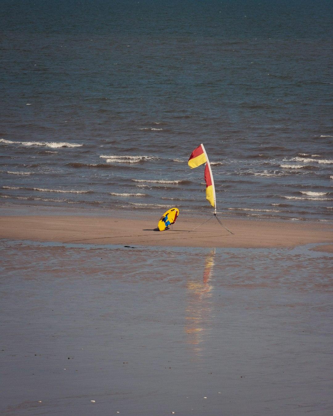 Flaga ratownicza i żółty bodyboard na mokrej plaży przy morzu.