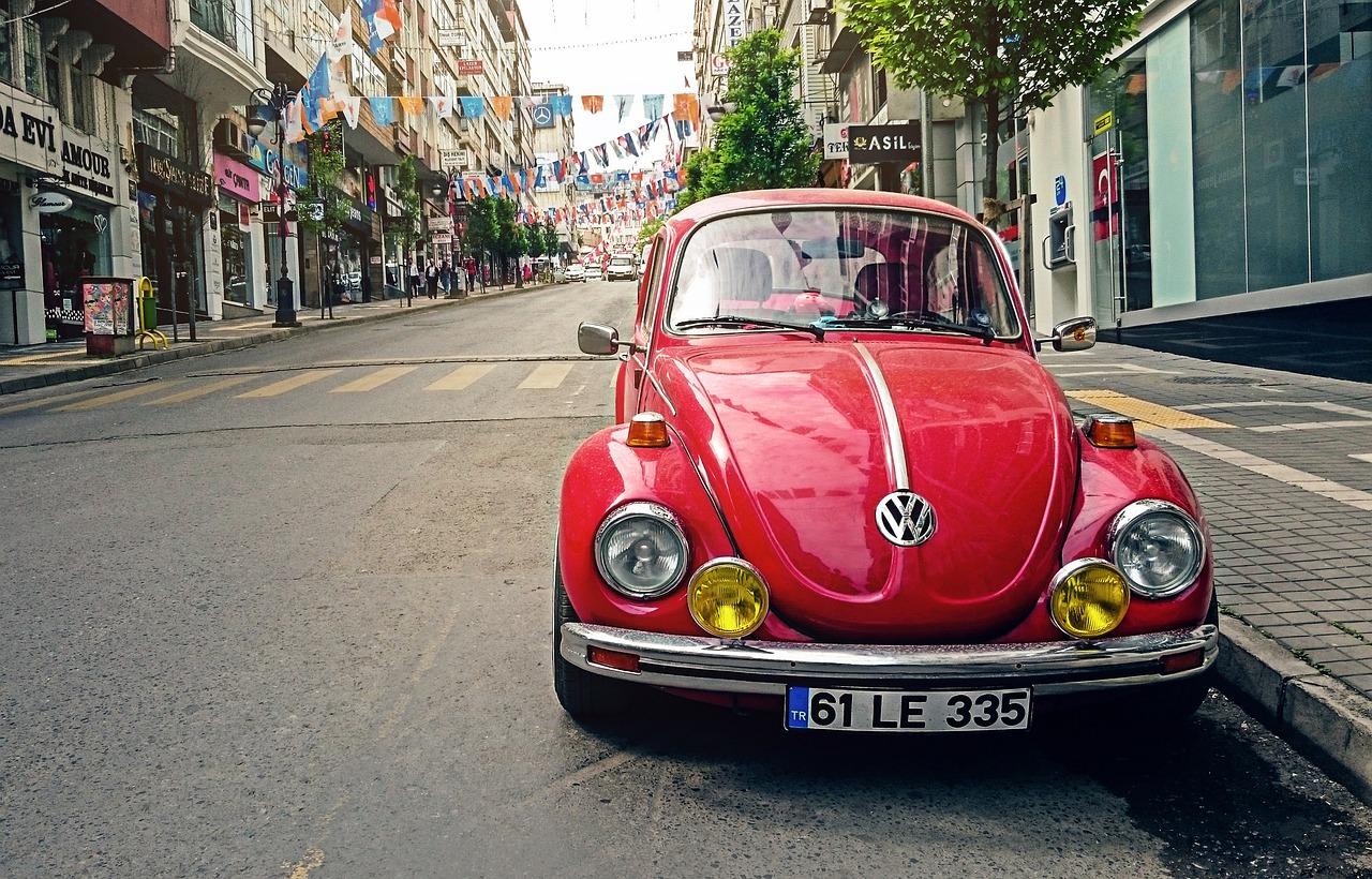 Czerwony klasyczny Volkswagen Garbus zaparkowany na ulicy tureckiego miasta z flagami.