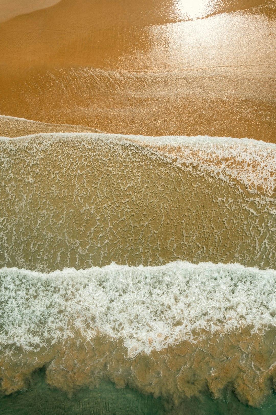 Widok z góry na piaszczystą plażę i spienione fale oceanu.