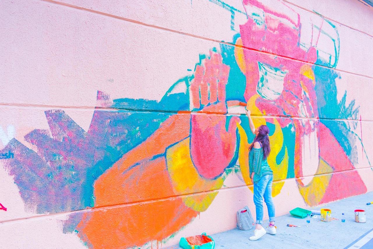 Kobieta malująca żywy mural street art na różowej ścianie.