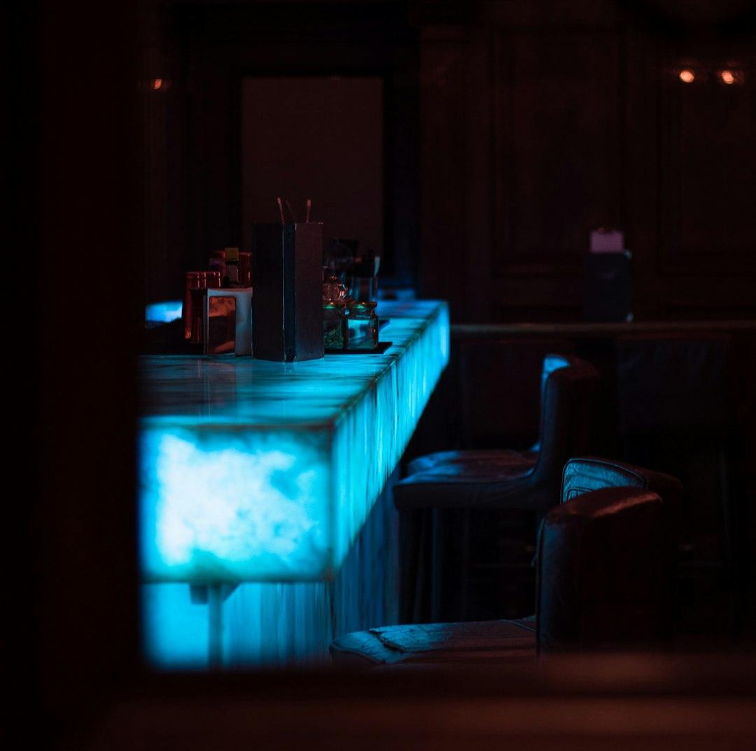 Ciemny bar z podświetlaną na niebiesko ladą i stołkami.