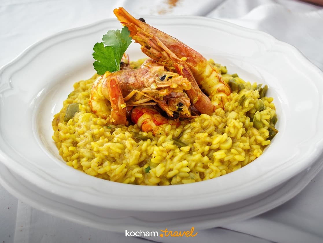Risotto z krewetkami i świeżą natką pietruszki na białym talerzu.