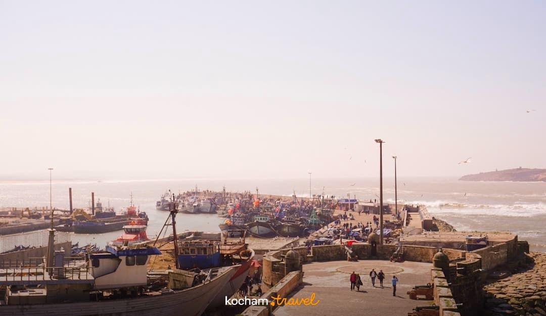 Tętniący życiem port rybacki, łodzie, falujące morze, kamienna promenada.