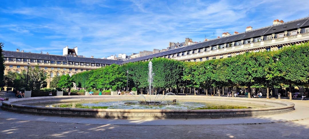 Paryski park z fontanną, zielonymi drzewami i zabytkową kamienicą.