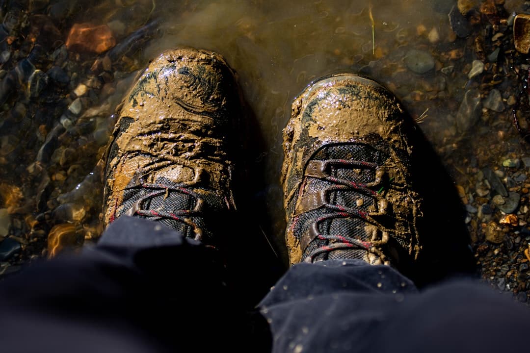 Zabłocone buty trekkingowe w płytkiej wodzie z kamieniami.