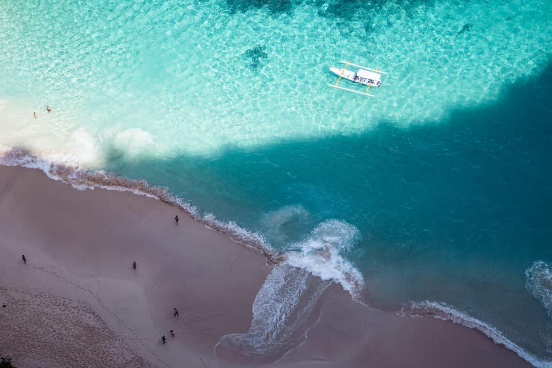 Tropikalna plaża z turkusową wodą, łodzią i spacerującymi ludźmi.
