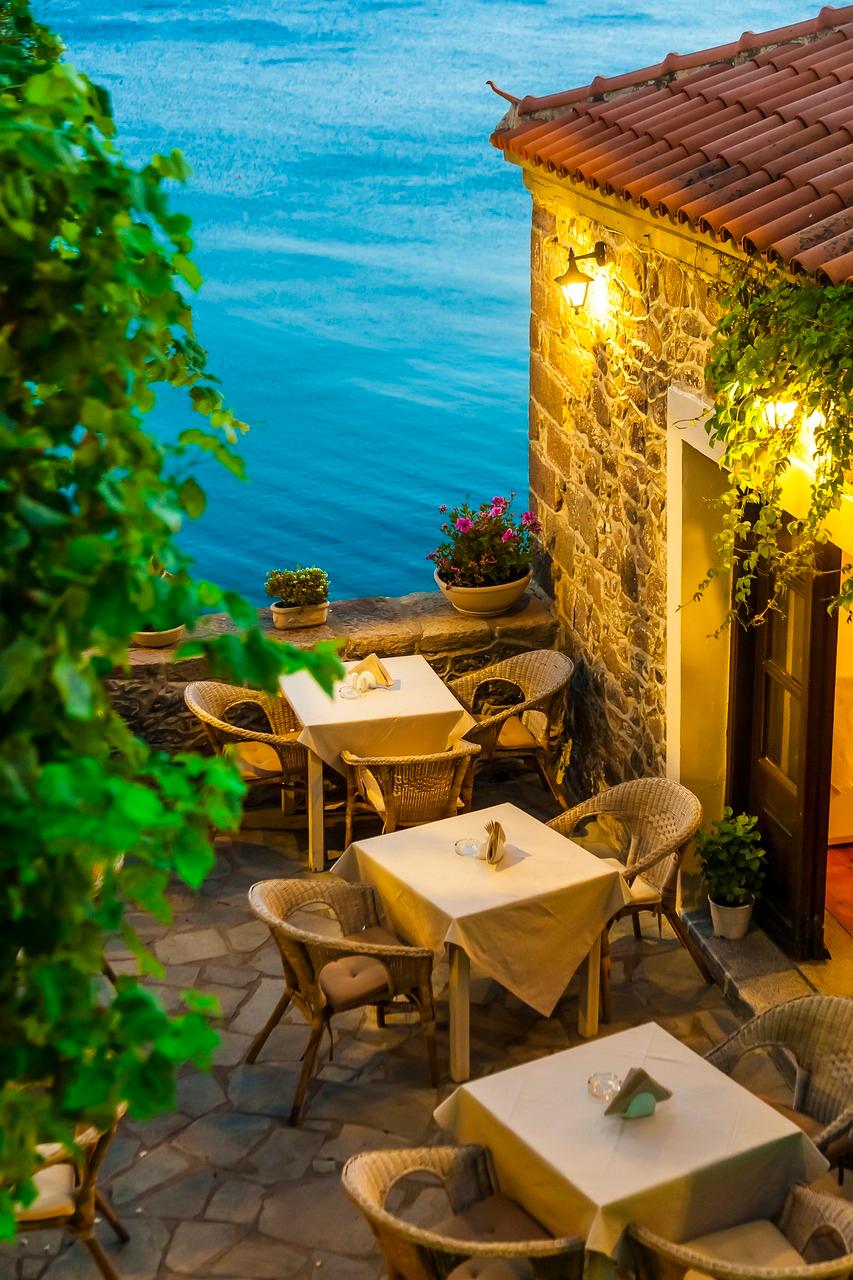 Wieczorne patio restauracji z widokiem na błękitne morze i kamienny budynek