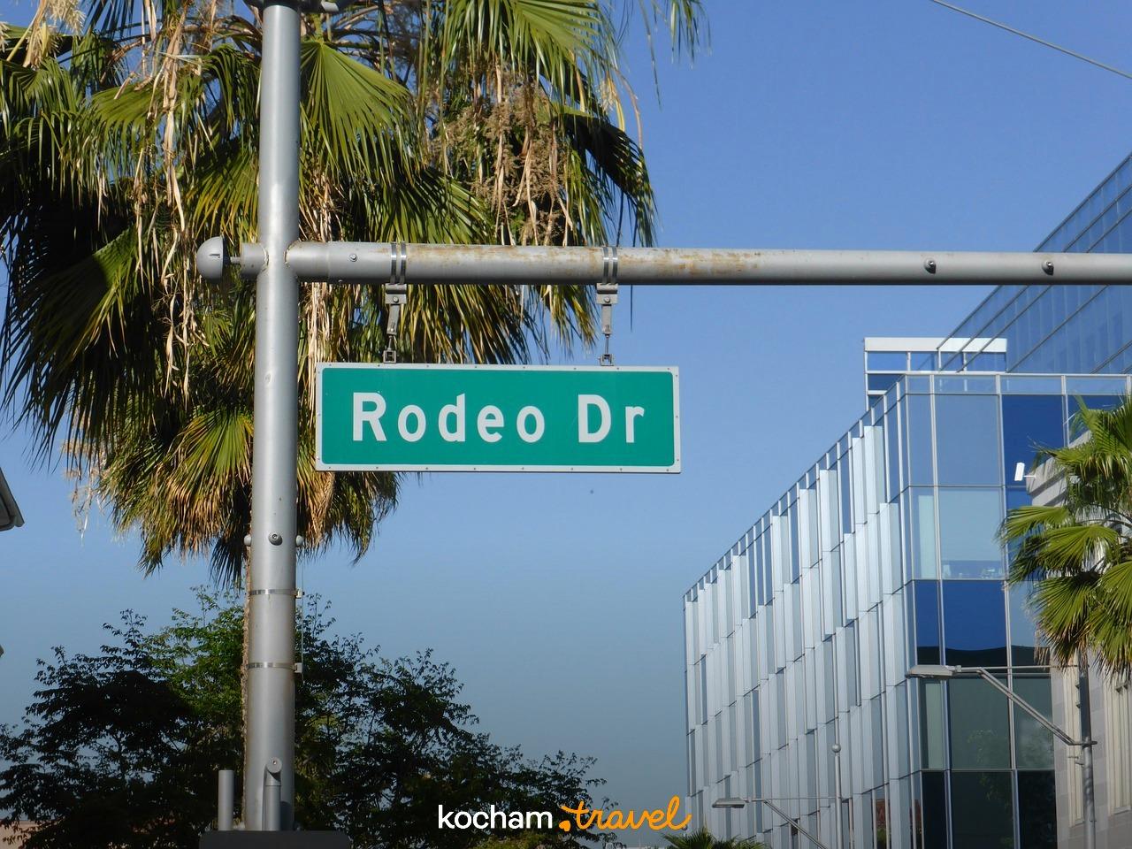 Znak ulicy Rodeo Drive, palmy, nowoczesny budynek w słońcu.